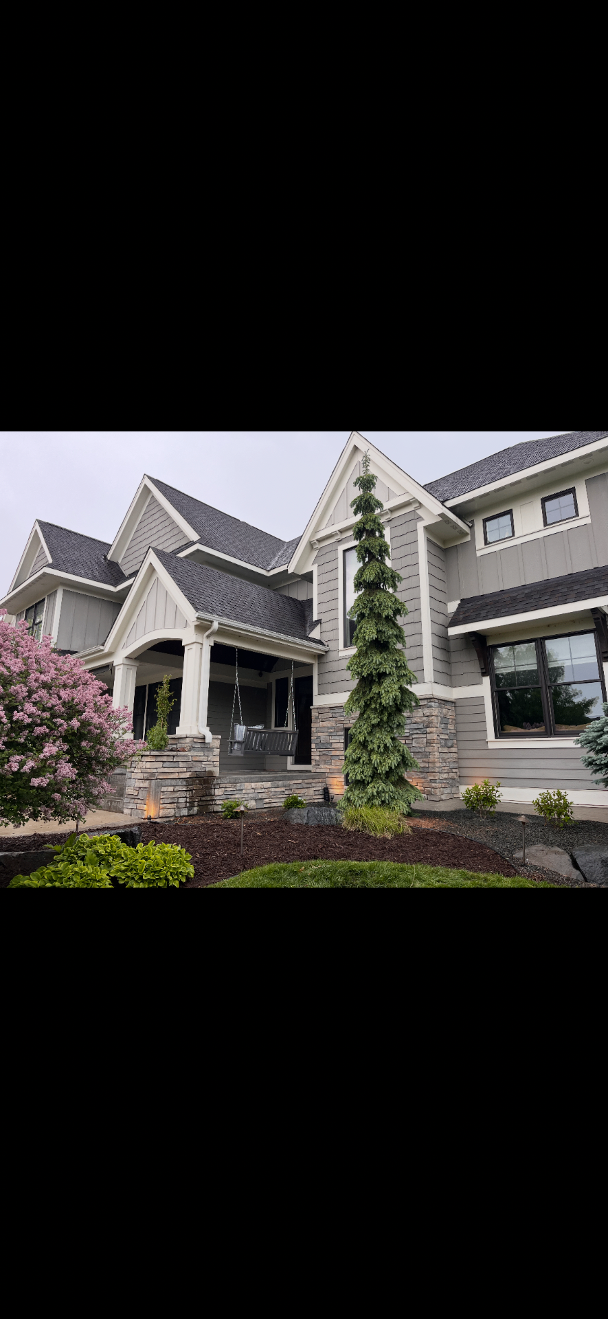 Front entry landscape with stacked stone, mulch bed, and spiral evergreen accent tree